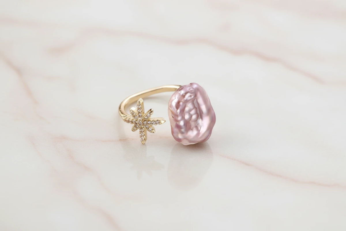 Goldener Sternenstaub-Perlenring von flyliving mit einem großen, rosa Barockperlen-Akzent.