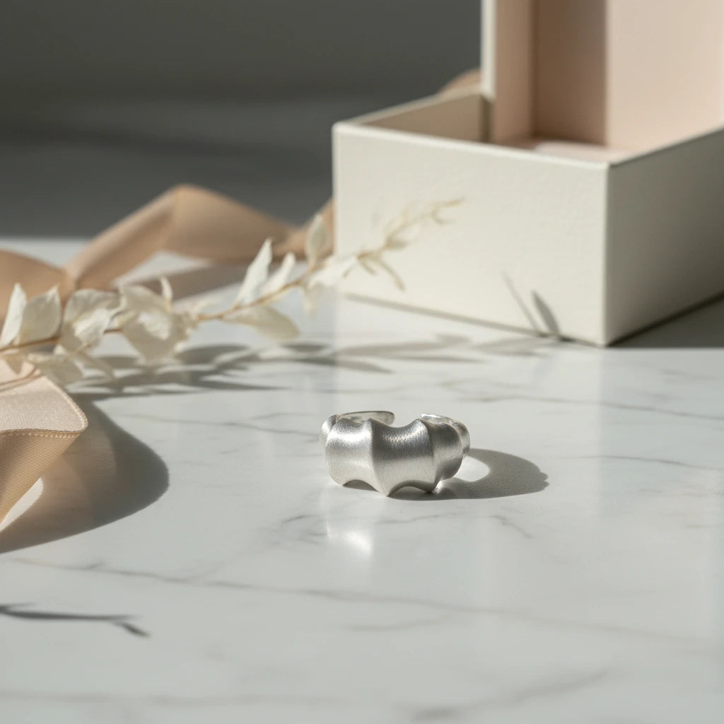 Silberfarbener Statement-Ring aus Metall von flyliving, mit organisch anmutender Form auf einem Marmortisch.
