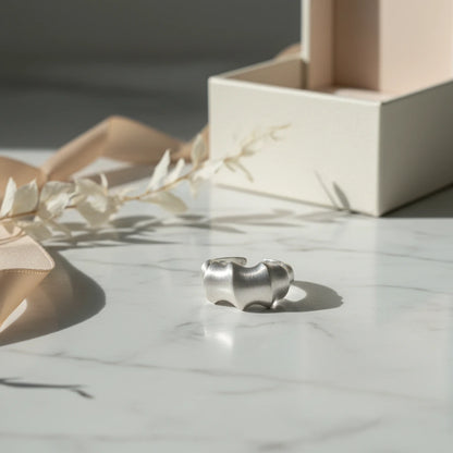 Silberfarbener Statement-Ring aus Metall von flyliving, mit organisch anmutender Form auf einem Marmortisch.
