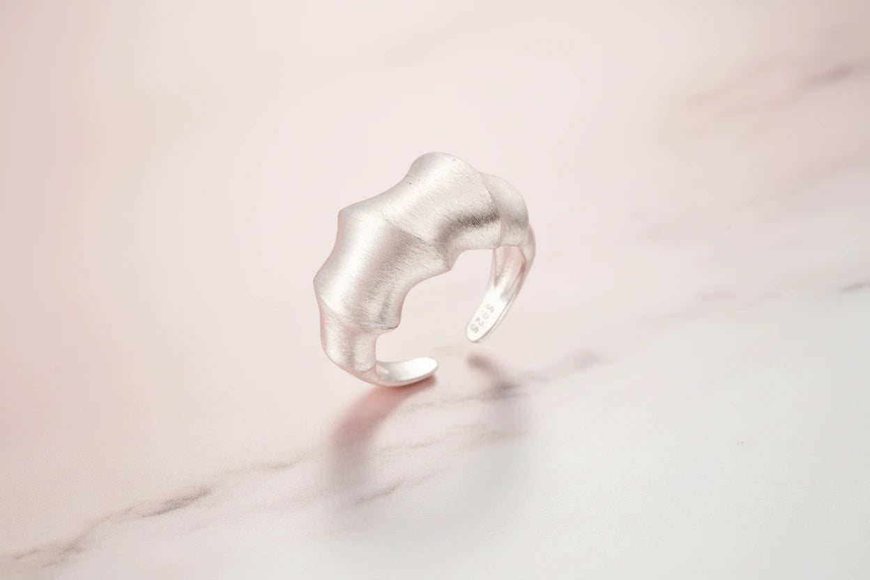 Statement-Ring aus flüssigem Silber von flyliving, mit matter Textur auf marmorierter Oberfläche.