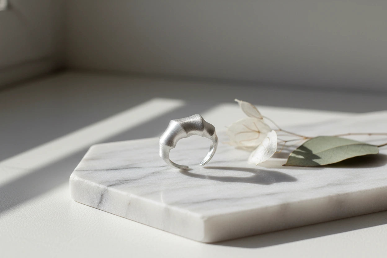 Silberfarbener Statement Ring aus Sterlingsilber von flyliving, auf Marmorplatte mit getrockneten Blumen.
