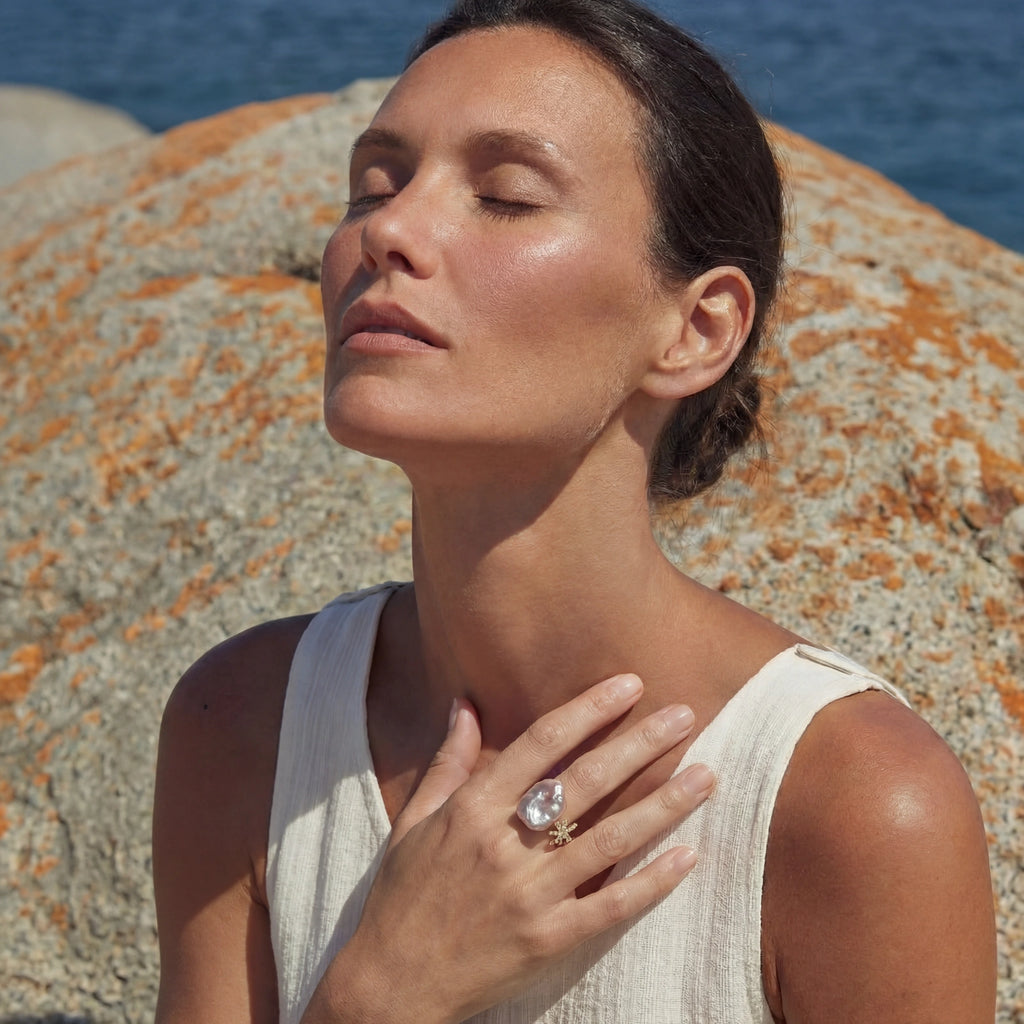 Perlenring Sternenstaub von flyliving, getragen an der Hand einer Frau, mit goldenem Sternendetail und großem, unregelmäßigem Perlenstein.