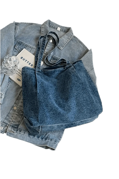 Eine Handtasche „Blue Jeans“, Größe M für Damen, von flyliving liegt auf einer flach hingelegten Jeansjacke, daneben ein Heft mit der Aufschrift „BUTTER“ und ein durchsichtiger Plastikgegenstand.