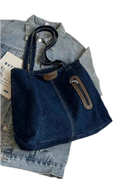 Die flyliving Handtasche „Blue Jeans“, medium, für Frauen, ist eine dunkelblaue Denim-Tote mit braunen Akzenten, Frontreißverschlussfach, zwei Henkeln und dezentem Logo – platziert auf einer hellblauen Jeansjacke.