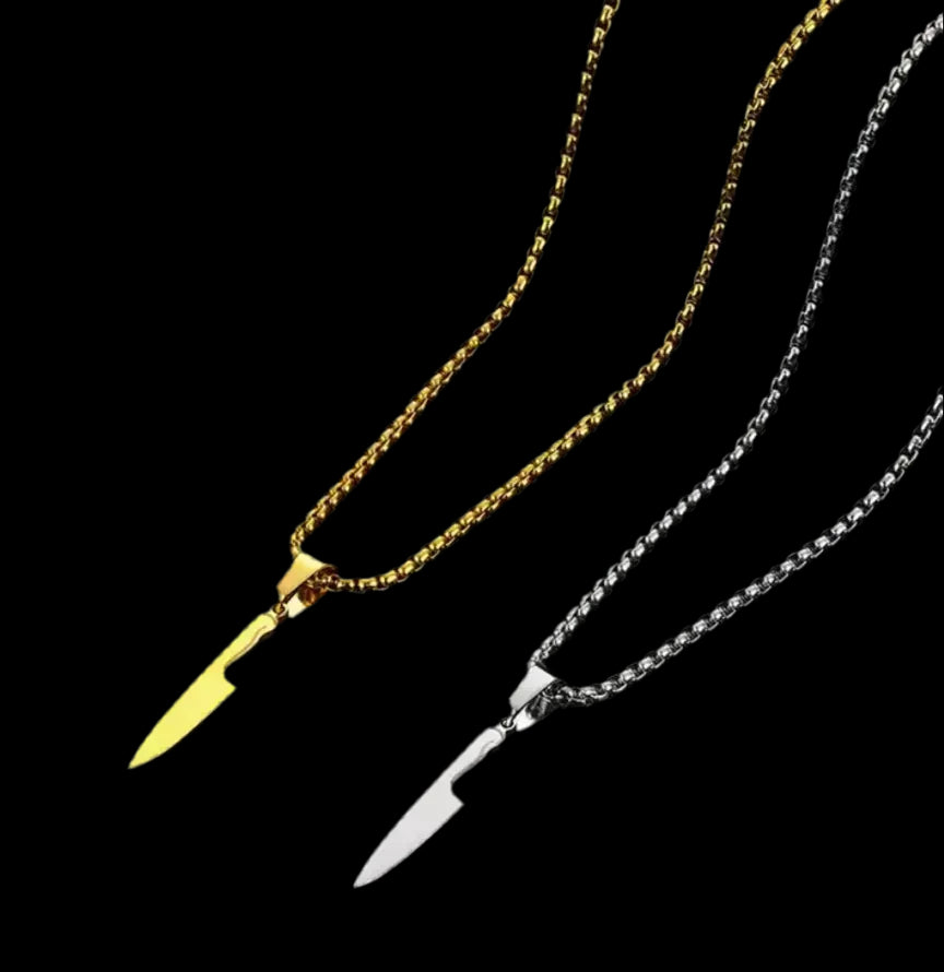 "Zwei „Laura“ Halsketten von flyliving auf schwarzem Hintergrund: eine goldene und eine silberne, jeweils mit einem Chefmesser-Anhänger aus Edelstahl. Stylischer Buttermesser-Ersatz für Kochfans."