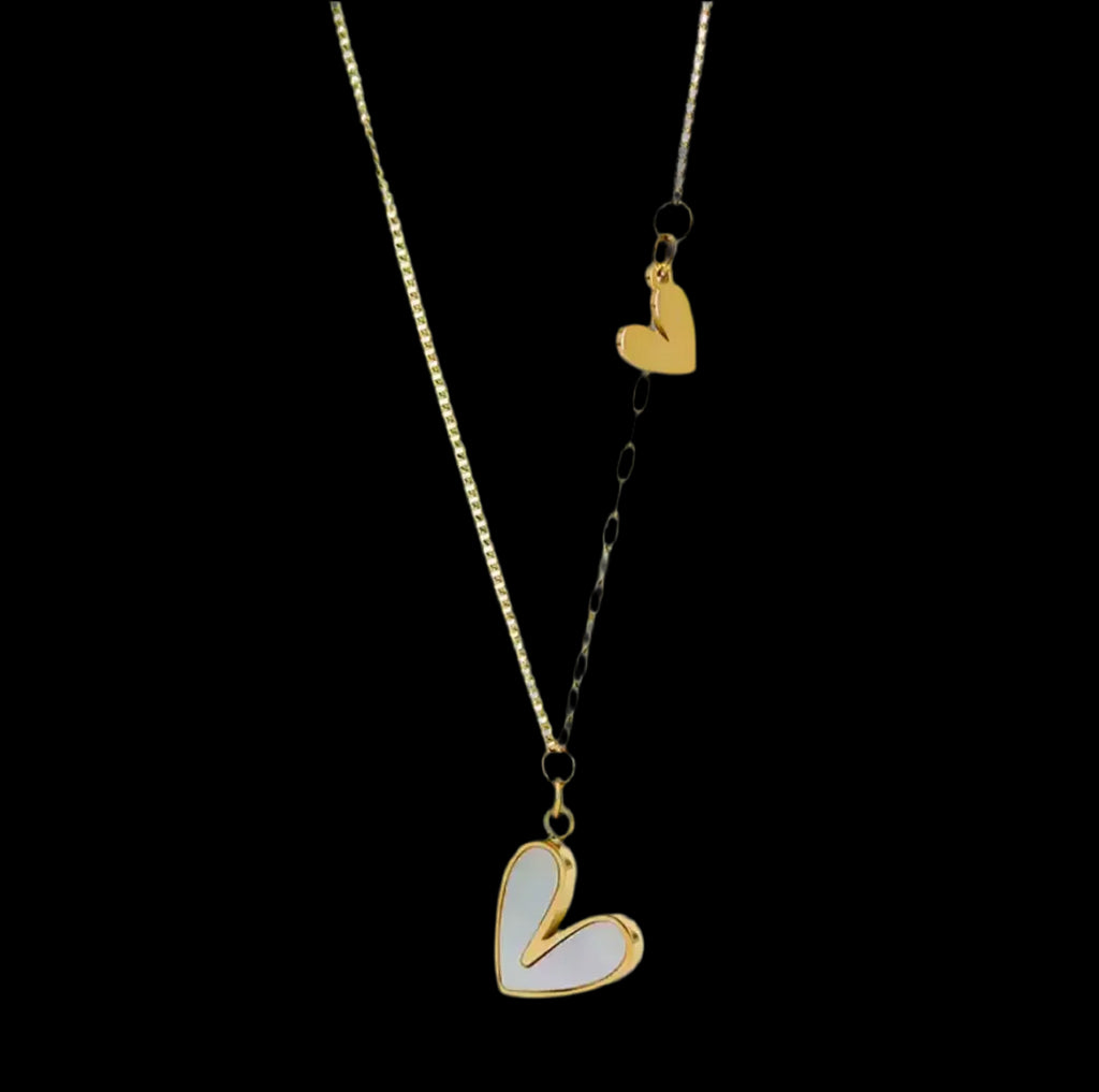 "Die goldene Halskette „Uschi“ von flyliving präsentiert zwei Edelstahl-Herzan-Anhänger, ein größeres mit Muscheleinlage und ein kleineres, an einer filigranen Kette – stilvoll inszeniert vor schwarzem Hintergrund."