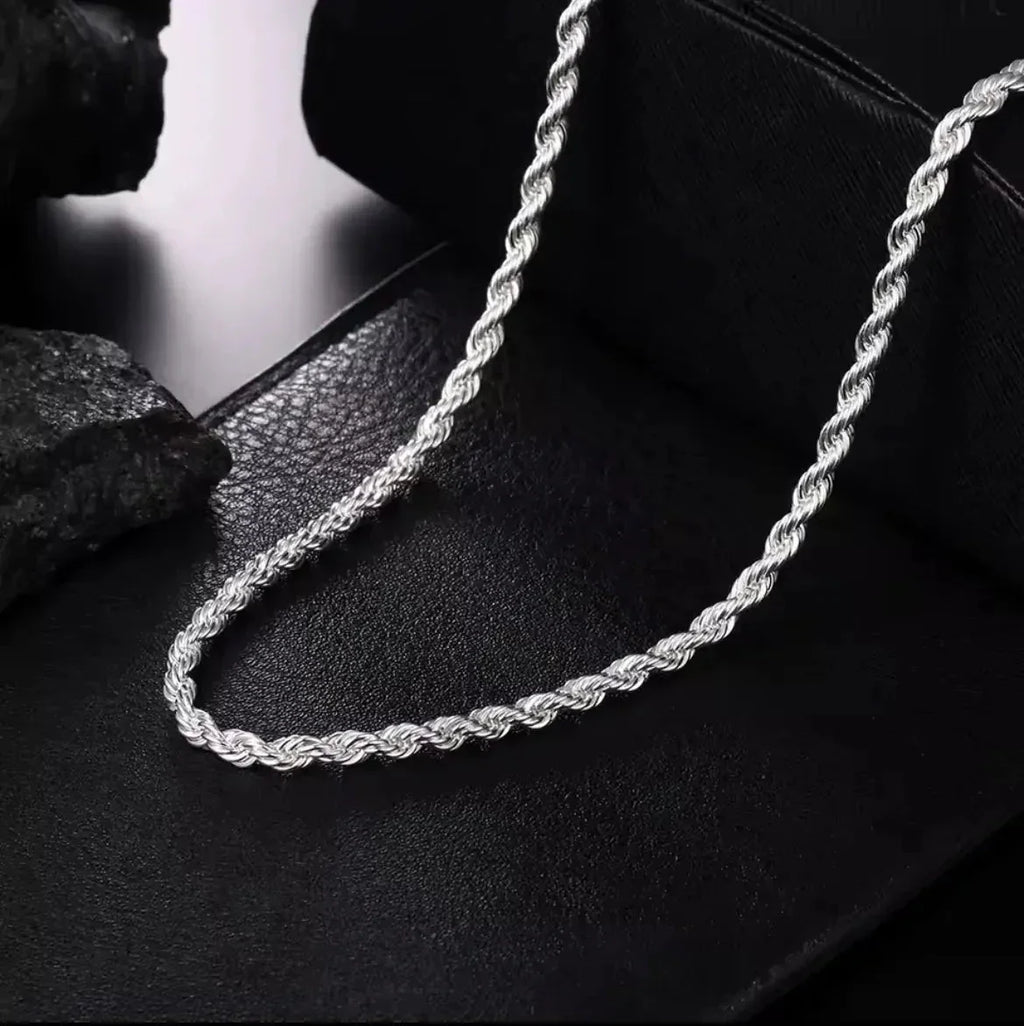 "Die Halskette „Helga“ aus Silber von flyliving mit filigran gedrehtem Design liegt auf schwarzem Leder, während dunkle Steine im Hintergrund die elegante Gliederkette stilvoll in Szene setzen."