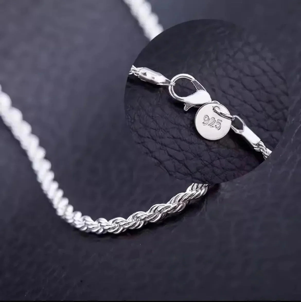 "Eine Nahaufnahme der Halskette „Helga“ aus Silber von flyliving auf schwarzem Leder. Ein Zoom zeigt den Karabinerverschluss und ein kleines rundes Etikett mit der Prägung 925, was bedeutet, dass es sich um Sterlingsilber handelt."