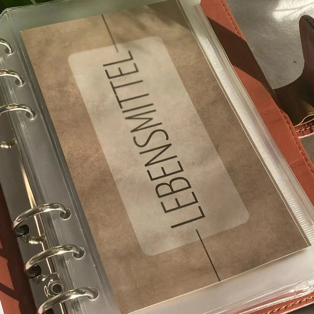 Eine Nahaufnahme des BeginnerBudget Grundausstattung Budget Planung von Budget Binder zeigt laminiertes braunes Papier und einen Ledereinband mit der Aufschrift "LEBENSMITTEL", wobei das Sonnenlicht einen Schatten wirft - ideal für die Umschlagmethode zum Budgetieren.