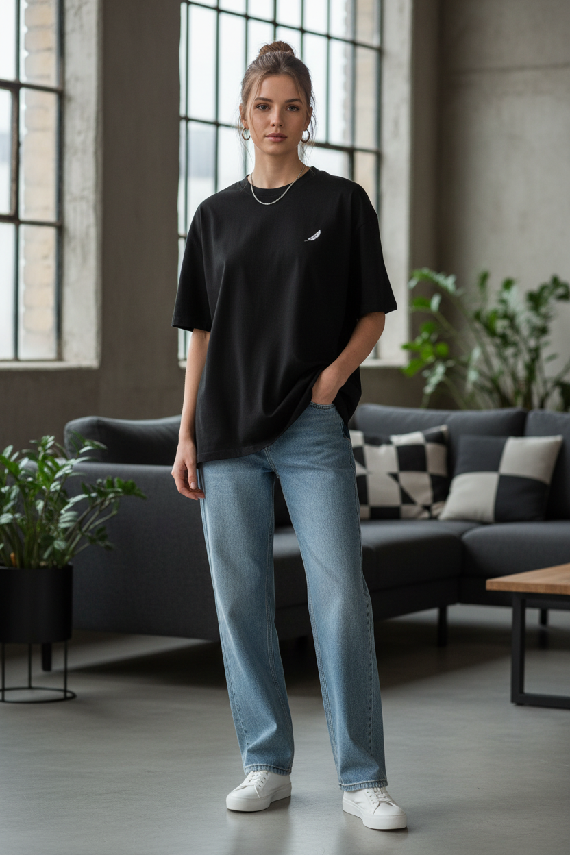 Black oversized unisex T-shirt by flyliving with a small white feather logo, styled casually with light blue jeans.