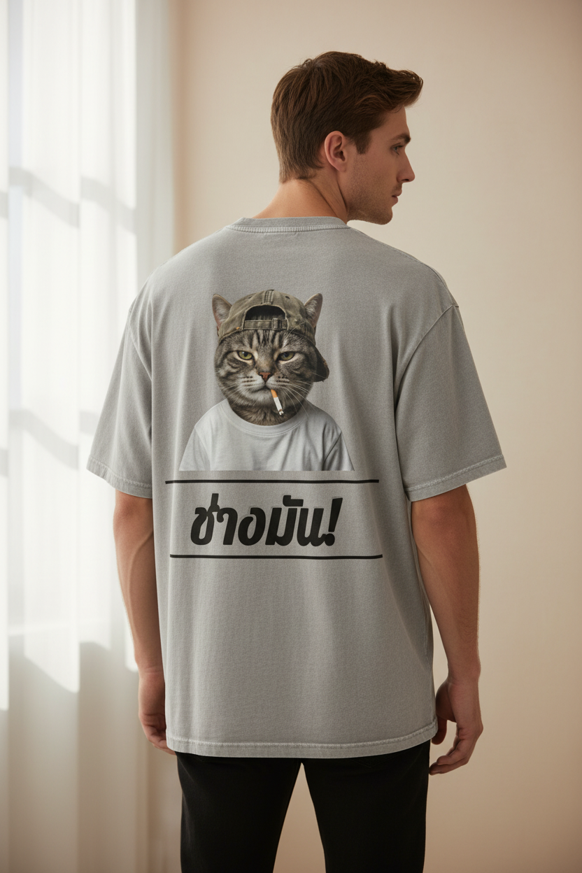 Grey oversized unisex t-shirt by flyliving featuring a smoking cat in a cap and the Thai phrase 'F*ck it!', seen from the back.
