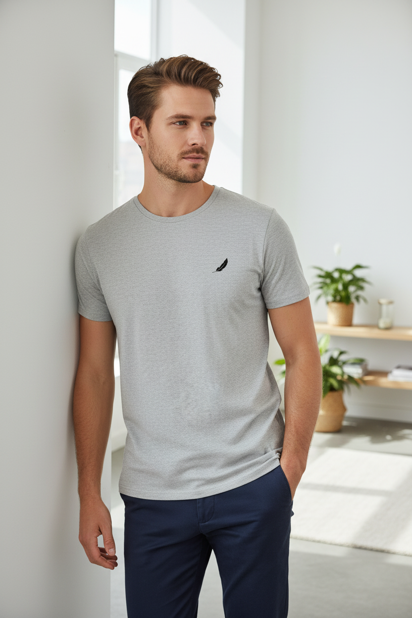 Premium organic grey crew neck T-shirt by flyliving with a black feather logo on the chest, worn by a man in navy chinos.