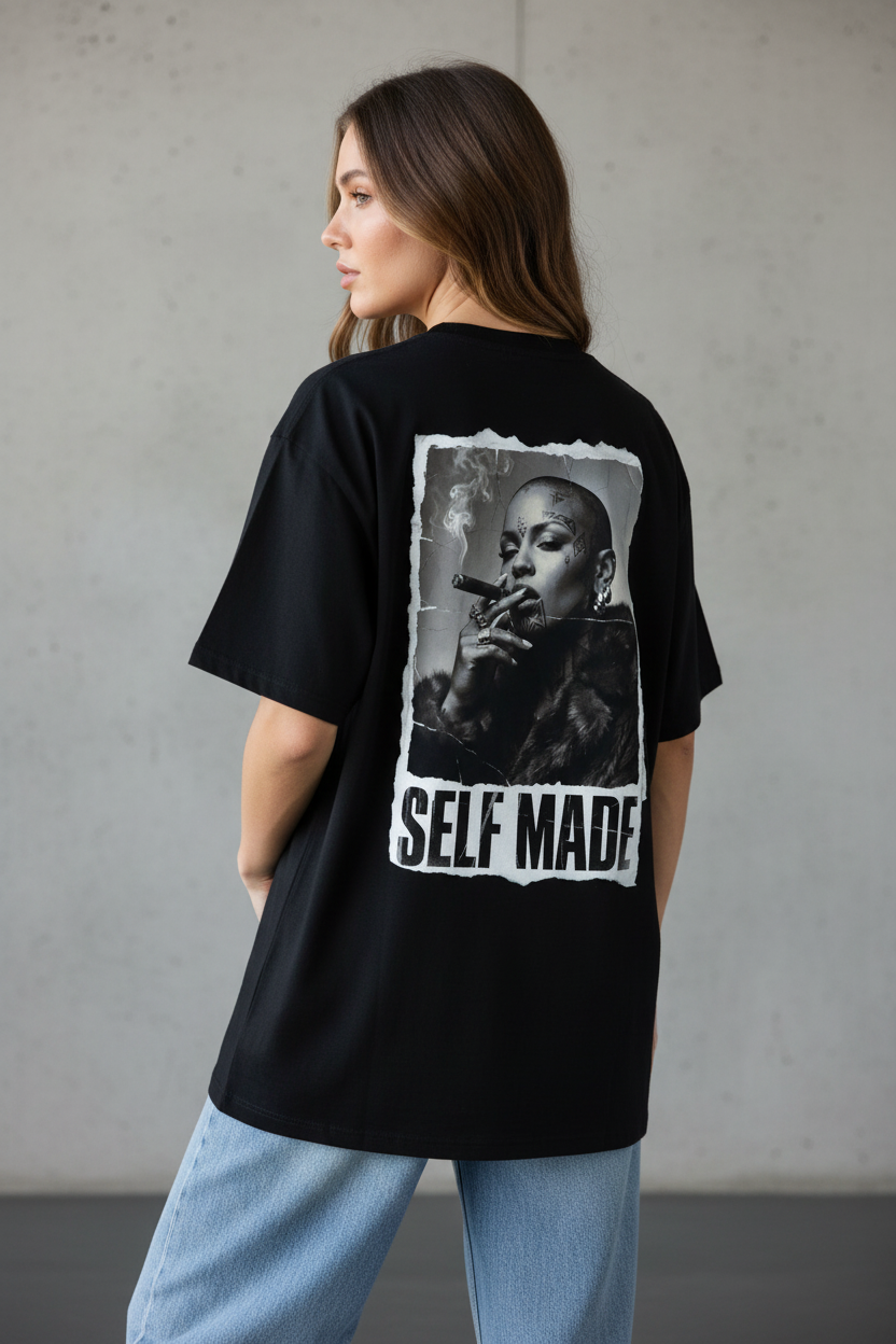 Black oversized T-shirt by flyliving, seen from the back, featuring a distressed print of a bald, tattooed woman smoking a cigar and "SELF MADE" text.
