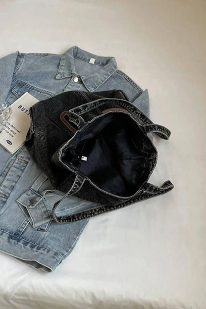 Eine flyliving Handtasche „Blue Jeans“ (medium, für Frauen), eine robuste Denimjacke und ein gefaltetes Blatt Papier liegen auf weißem Untergrund; Die Handtasche ruht oben auf der Jacke.