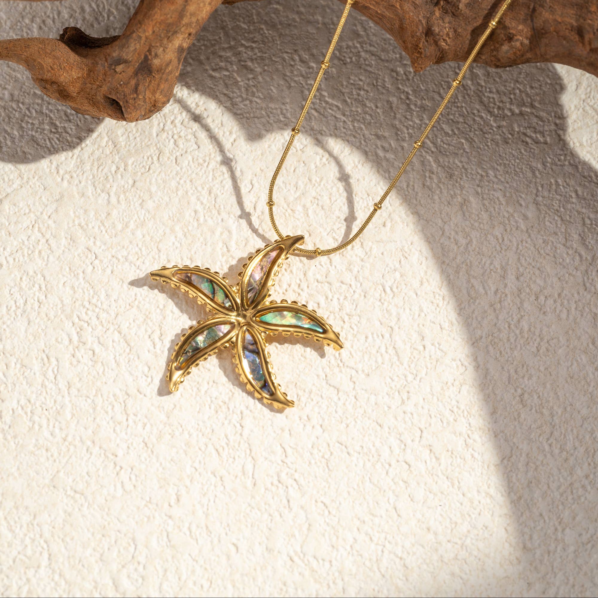 Golden stainless steel starfish necklace with iridescent mother-of-pearl by flyliving, featuring a delicate beaded chain on a textured surface.