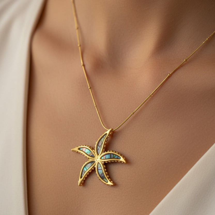 Gold-toned stainless steel starfish necklace with iridescent mother-of-pearl inlay by flyliving, on a delicate beaded chain, worn by a model.