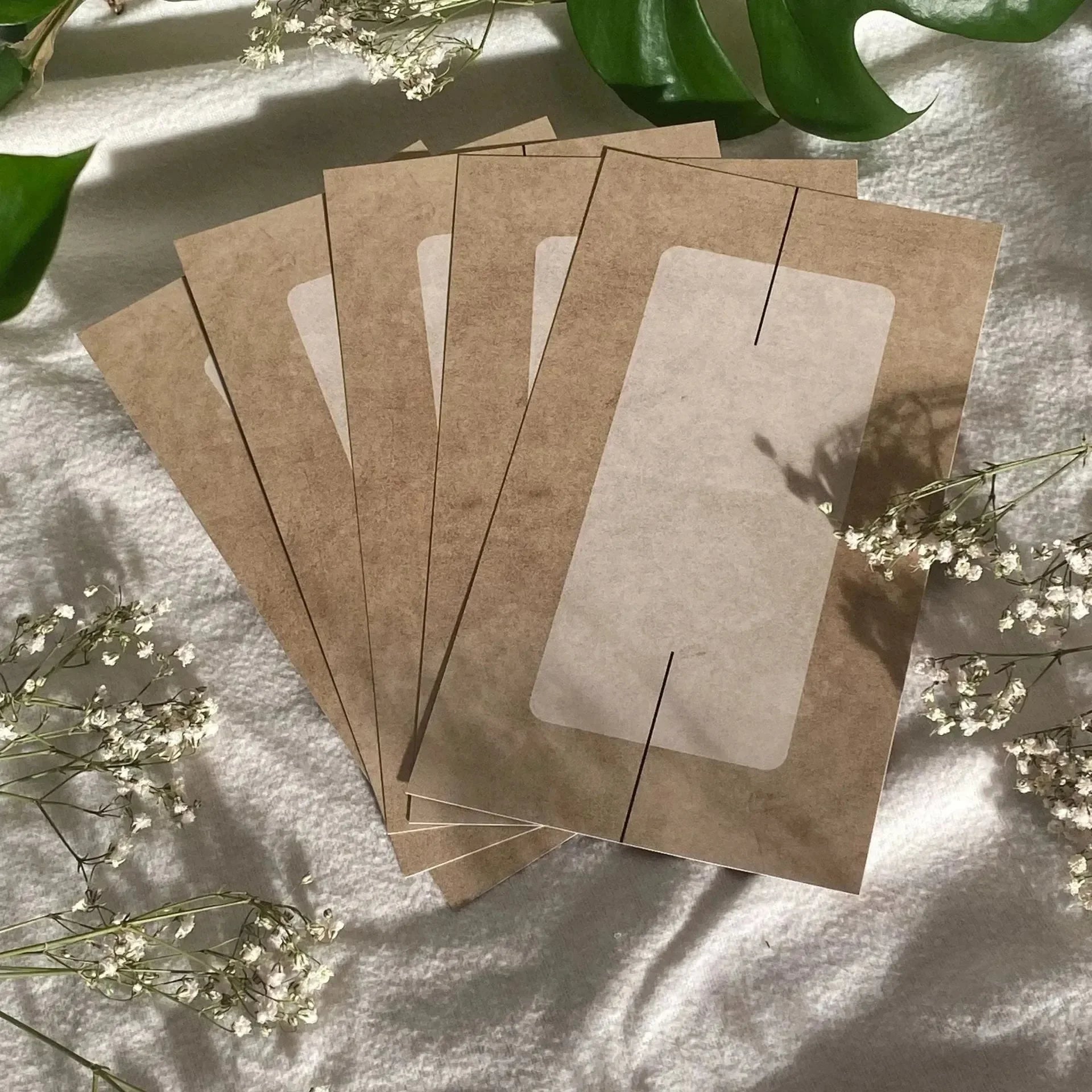 Vier Blanko Dashboards von BeginnerBudget (4er-Pack) liegen fächerförmig auf hellem Stoff, umgeben von weißen Blüten und grünen Blättern - perfekt für individuelle Beschriftung oder als Zipperumschläge im A6 Binder.