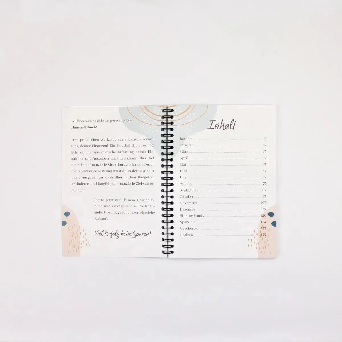 Der BeginnerBudget Budget Planer (Jahresunabhängig), DIN A5, liegt aufgeschlagen auf einer weißen Fläche und zeigt einen deutschen Willkommensgruß und monatliche Inhalte mit minimalem abstraktem Design in Beige und Pfirsich.