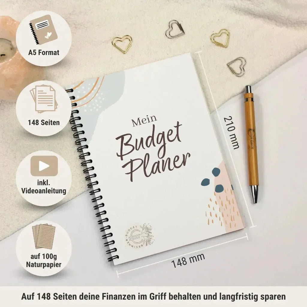Der BeginnerBudget Budgetplaner (Jahresunabhängig) - DIN A5 mit 148 Seiten, Videoanleitung, Sinking-Funds-Teil und 100g Naturpapier ist spiralgebunden und liegt auf einem Schreibtisch neben einem goldenen Stift, goldenen herzförmigen Büroklammern und einem weißen Tuch.