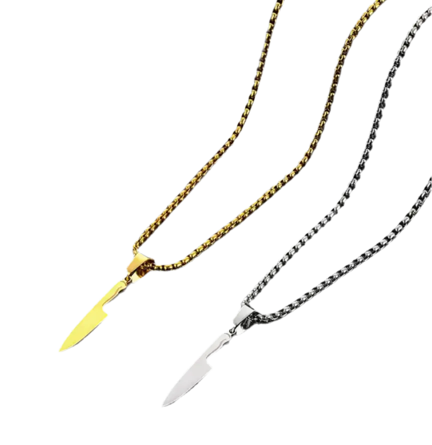 Zwei „Laura“ Halsketten von flyliving auf schwarzem Hintergrund: eine goldene und eine silberne, jeweils mit einem Chefmesser-Anhänger aus Edelstahl. Stylischer Buttermesser-Ersatz für Kochfans.