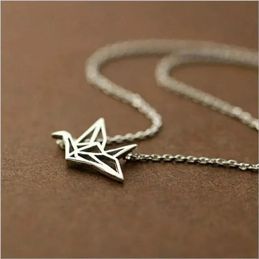 Die Halskette „Wilhelm“ von flyliving – ein filigraner Kranich-Anhänger aus 925er Silber im Origami-Stil – liegt auf einer braunen Fläche.