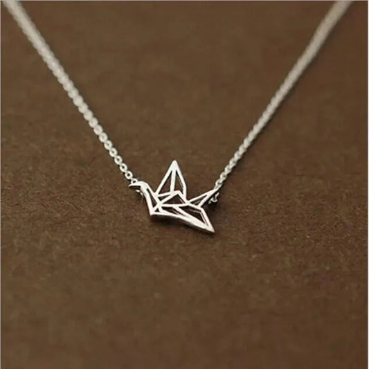 Die Halskette „Wilhelm“ von flyliving ist eine filigrane Silberkette mit Kranich-Anhänger aus 925 Sterling Silber, präsentiert auf braunem Hintergrund.