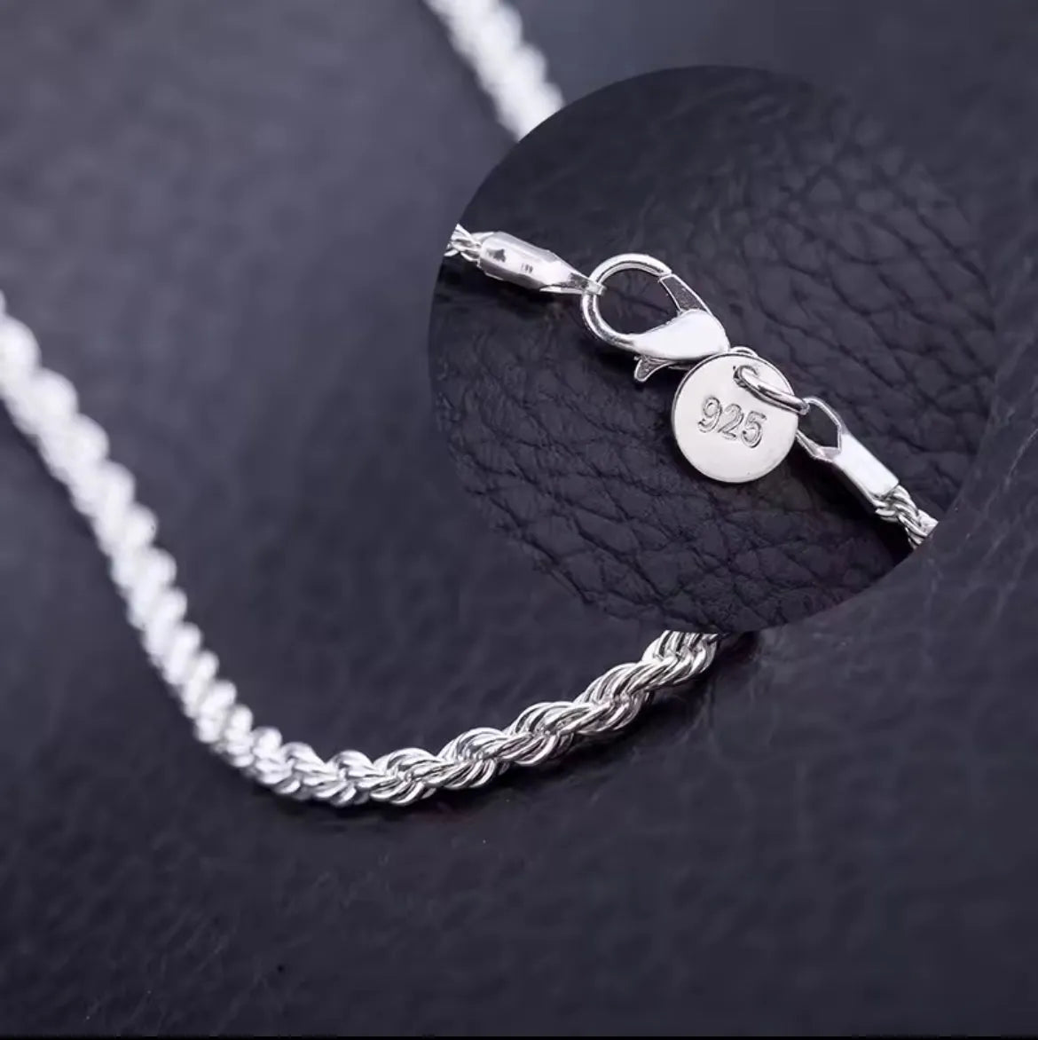 Eine Nahaufnahme der Halskette „Helga“ aus Silber von flyliving auf schwarzem Leder. Ein Zoom zeigt den Karabinerverschluss und ein kleines rundes Etikett mit der Prägung 925, was bedeutet, dass es sich um Sterlingsilber handelt.