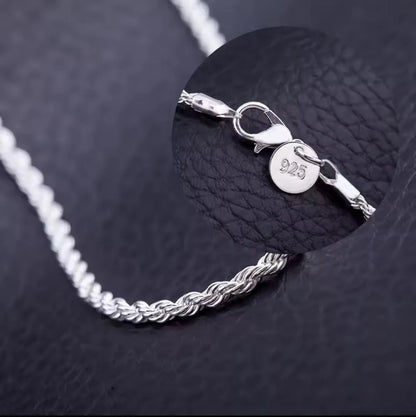 Eine Nahaufnahme der Halskette „Helga“ aus Silber von flyliving auf schwarzem Leder. Ein Zoom zeigt den Karabinerverschluss und ein kleines rundes Etikett mit der Prägung 925, was bedeutet, dass es sich um Sterlingsilber handelt.