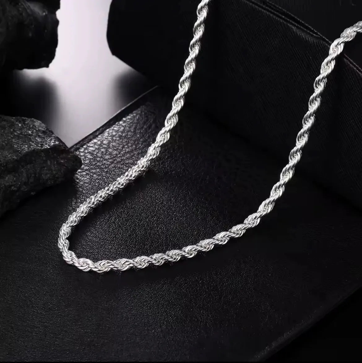Die Halskette „Helga“ aus Silber von flyliving mit filigran gedrehtem Design liegt auf schwarzem Leder, während dunkle Steine im Hintergrund die elegante Gliederkette stilvoll in Szene setzen.