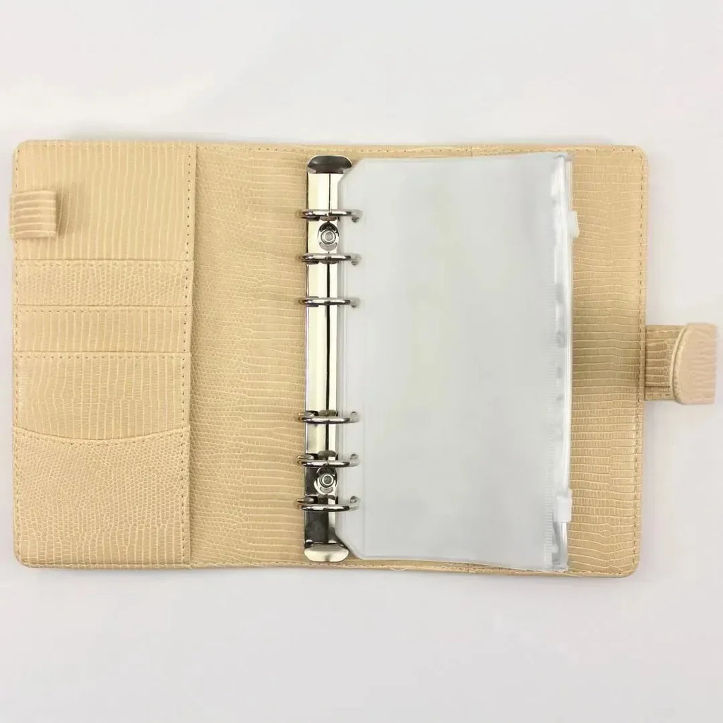 Der BeginnerBudget Budget Binder "Gecko" - Personal (A6) ist ein offener beigefarbener strukturierter Lederplaner mit einem Kunststoff-Binder, Kartenschlitzen auf der linken Seite, einer transparenten Kunststoff-Sparzierhülse in den Ringen, und ist leer auf einer weißen Oberfläche.