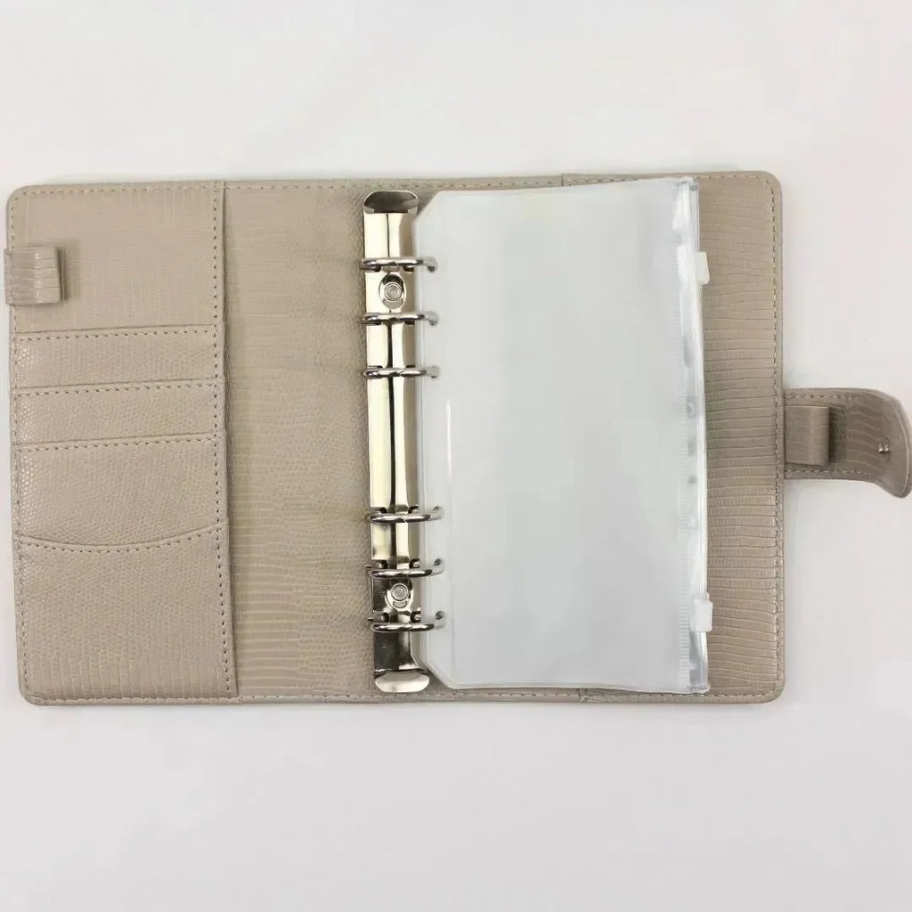 Der BeginnerBudget Budget Binder "Gecko" - Personal (A6) in beige ist offen auf einer weißen Oberfläche, mit Metallringen, durchsichtigen Plastikhüllen für Sparziele, Kartenfächern und einem Druckknopfverschluss auf der rechten Seite.