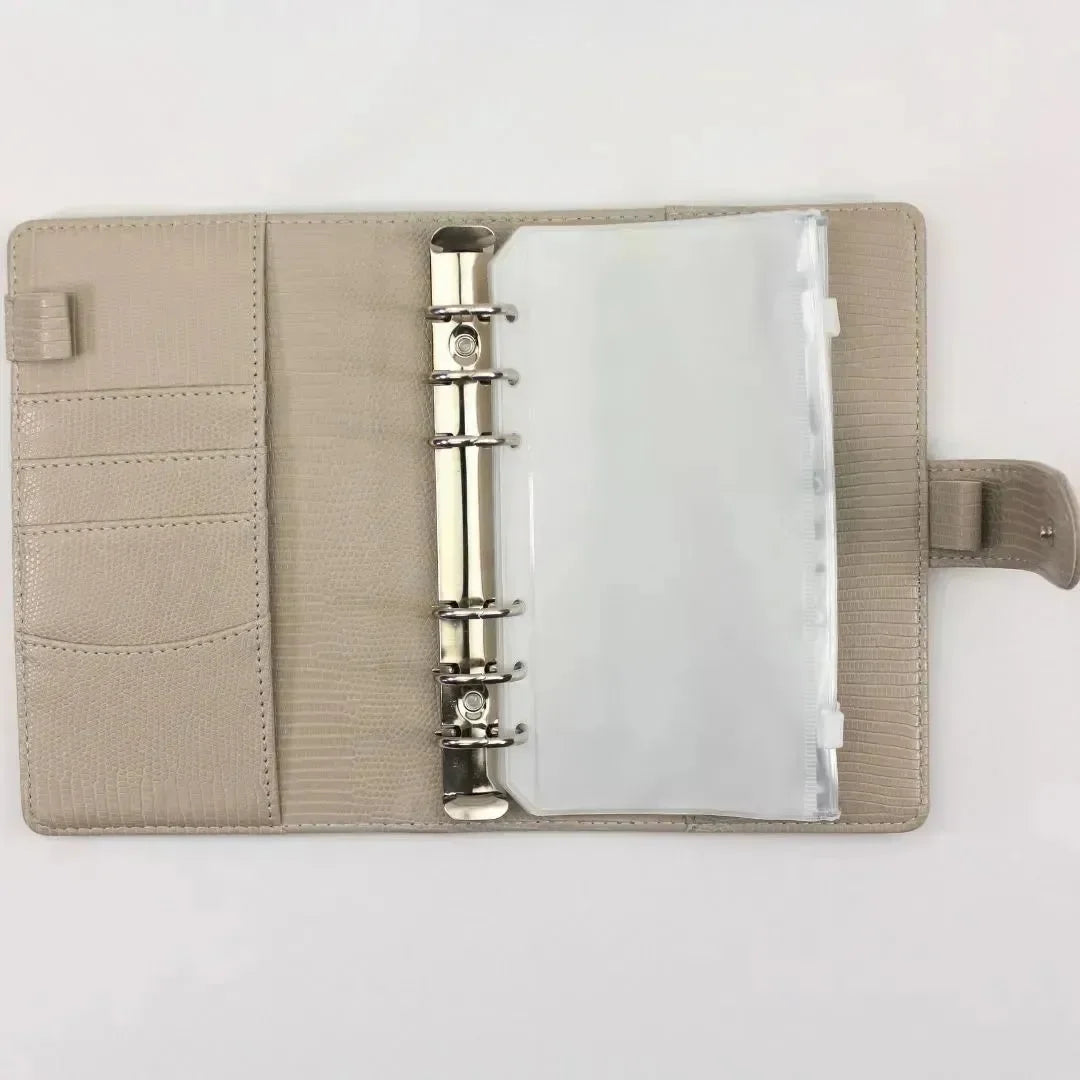 Der BeginnerBudget Budget Binder "Gecko" - Personal (A6) in beige ist offen auf einer weißen Oberfläche, mit Metallringen, durchsichtigen Plastikhüllen für Sparziele, Kartenfächern und einem Druckknopfverschluss auf der rechten Seite.