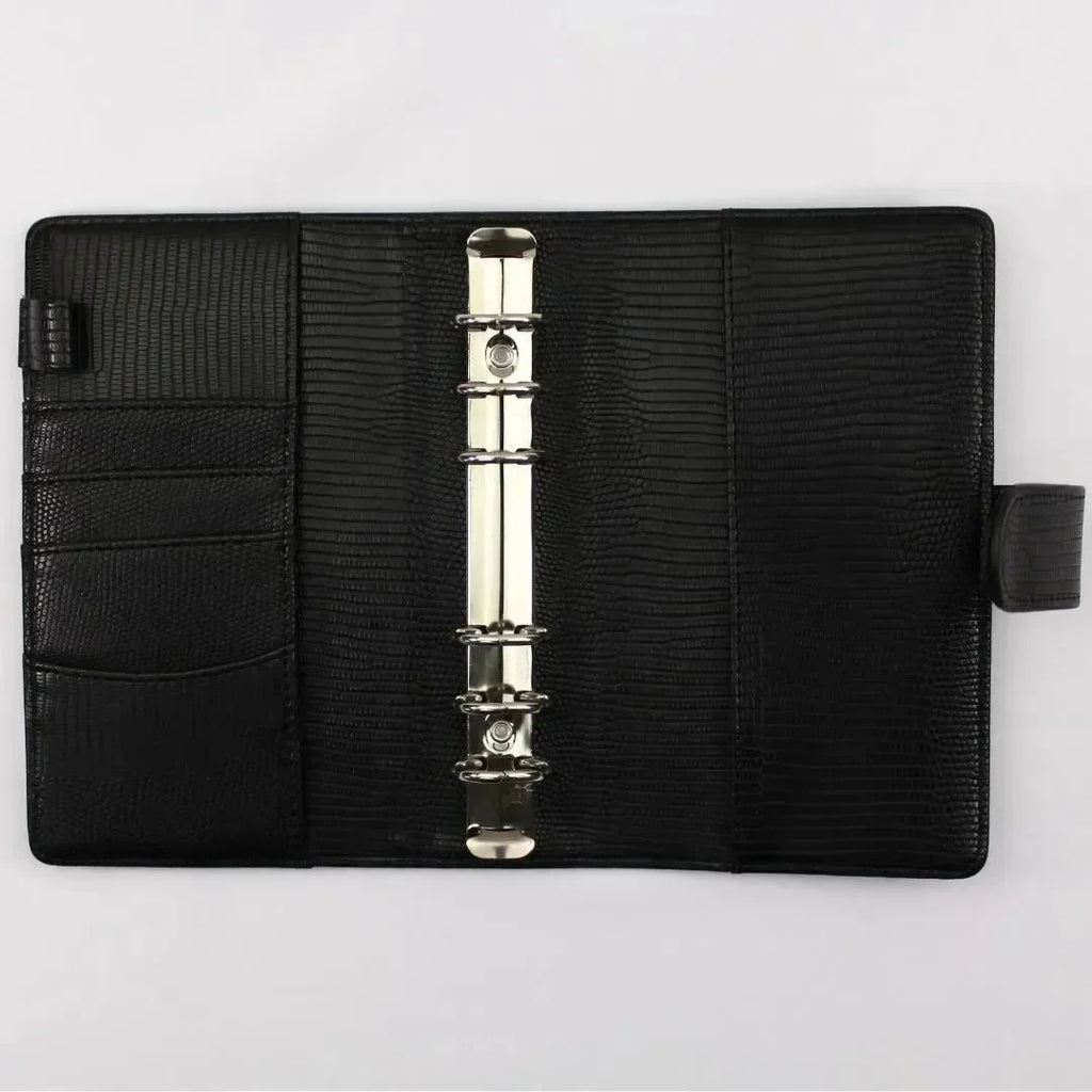 Der BeginnerBudget Budget Binder "Gecko" - Personal (A6) ist ein schwarzer, strukturierter Lederbinder mit einem Sechsring-Mechanismus, drei linken Innentaschen und einer Stiftschlaufe, offen auf einer weißen Oberfläche dargestellt.
