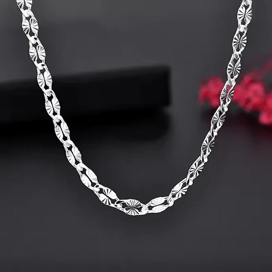 Eine Nahaufnahme der flyliving Halskette „Hildegard“ aus Silber mit einem detaillierten geometrischen Muster aus 925er Sterlingsilber auf einer dunklen Oberfläche mit einem zartroten Blumenakzent im Hintergrund.