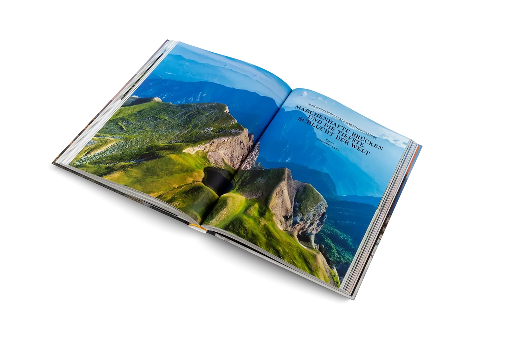 Das Buch "Wanderlust Mittelmeer" von gestalten EU Shop ist auf einem weißen Hintergrund aufgeschlagen und zeigt auf der rechten Seite ein Luftbild mit grünen Bergen unter blauem Himmel und deutschen Tourentipps.