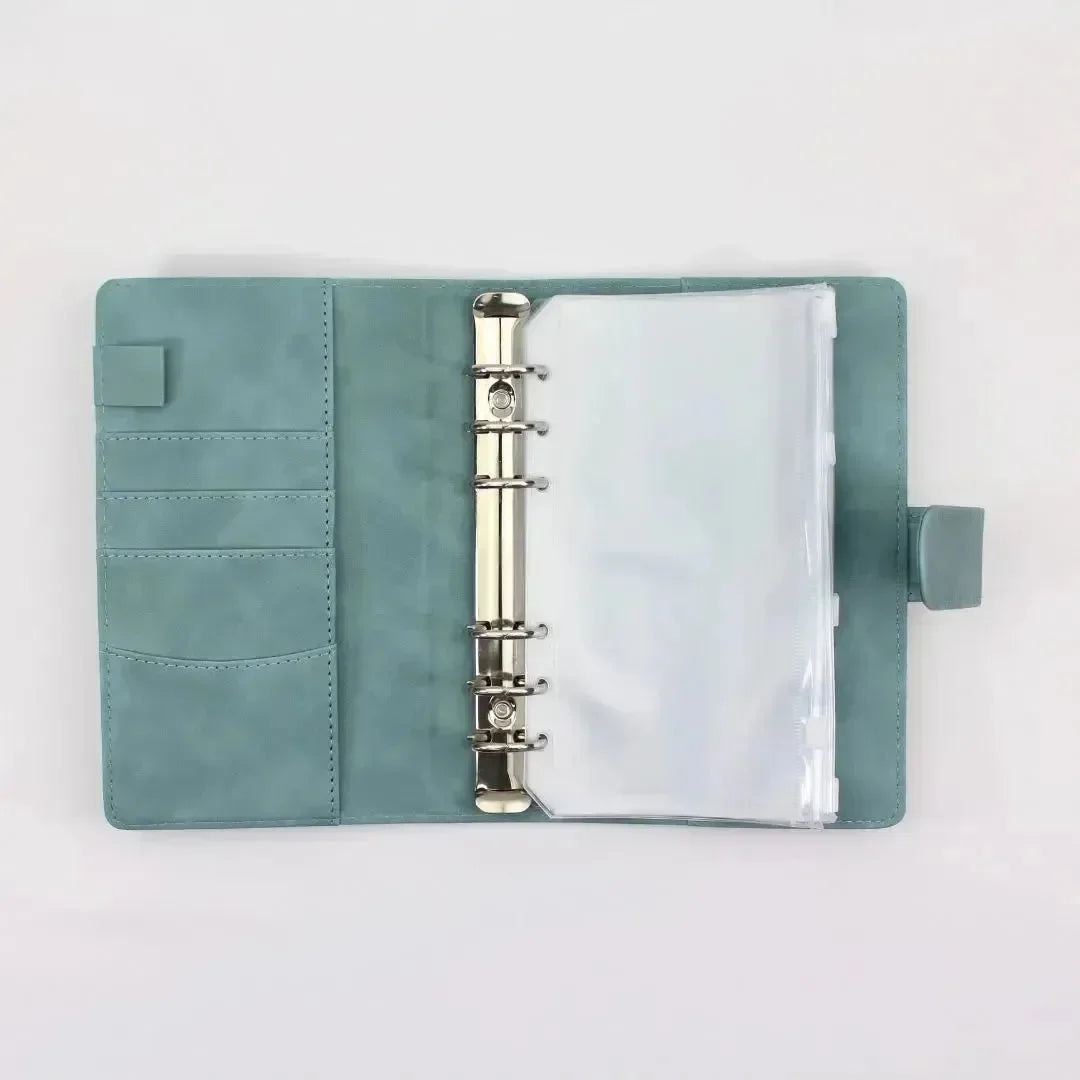 Der BeginnerBudget Budget Binder (veganes) Wildleder - Personal (A6) in teal verfügt über Metallringe mit Klarsichthüllen, Kartenfächer, eine Stiftschlaufe auf der linken Seite und eine Druckknopflasche auf der rechten Seite. Die lederähnliche Oberfläche ist auf einem schlichten weißen Hintergrund zu sehen.