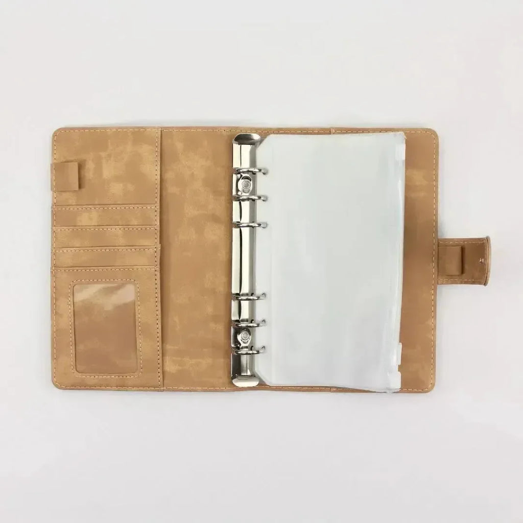 Der BeginnerBudget Budget Binder (veganes) Wildleder - Personal (A6) liegt aufgeklappt auf weißem Grund und zeigt links Metallringe mit Klarsichthüllen für die Finanzübersicht, Kartenschlitze und Ausweisfenster und rechts eine Druckknopf- oder Magnetverschlusslasche.