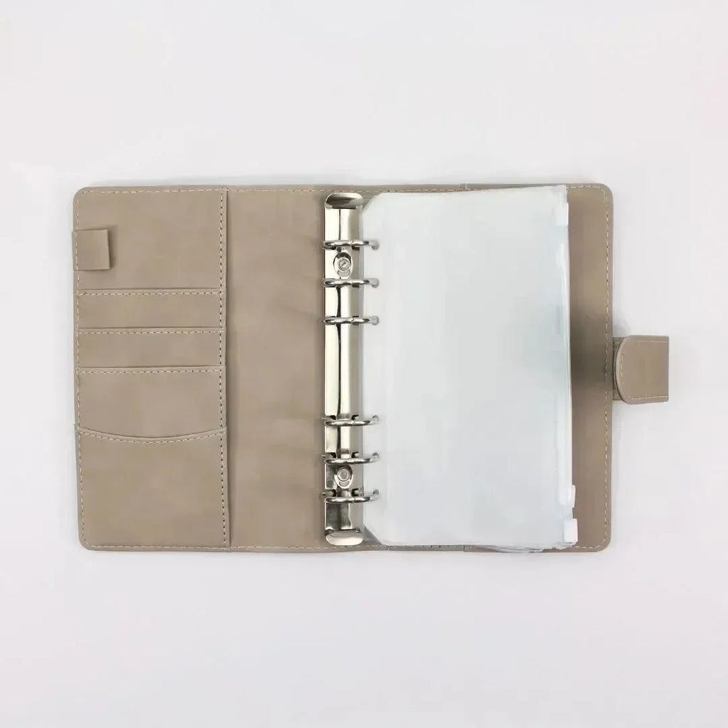 Der BeginnerBudget Budget Binder (veganes Wildleder - Personal, A6) in Beige ist offen, mit Metallringen, Klarsichthüllen und Kartenfächern auf der linken Seite - ideal zum Sparen oder für eine klare Finanzübersicht - und flach auf weißem Hintergrund.
