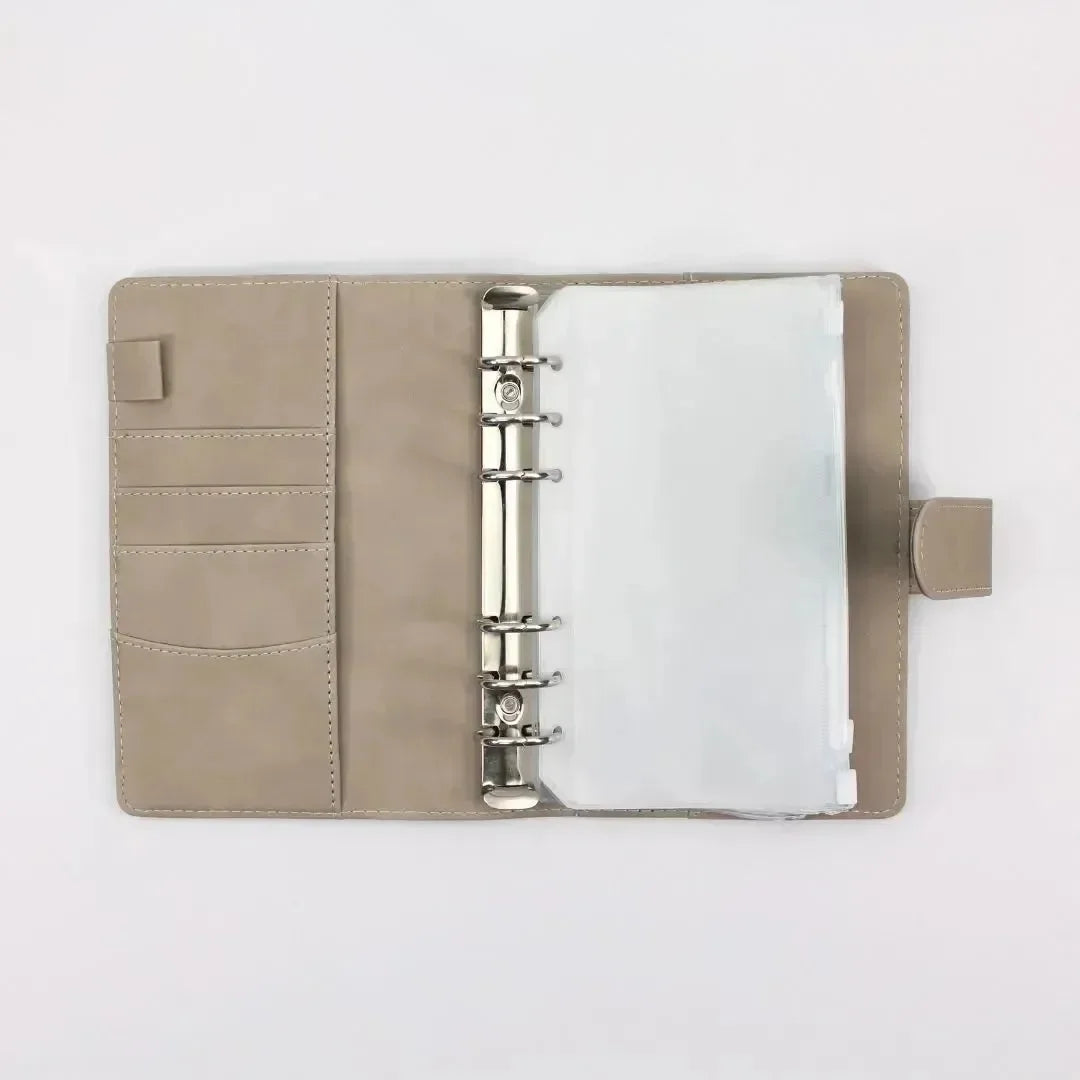 Der BeginnerBudget Budget Binder (veganes Wildleder - Personal, A6) in Beige ist offen, mit Metallringen, Klarsichthüllen und Kartenfächern auf der linken Seite - ideal zum Sparen oder für eine klare Finanzübersicht - und flach auf weißem Hintergrund.