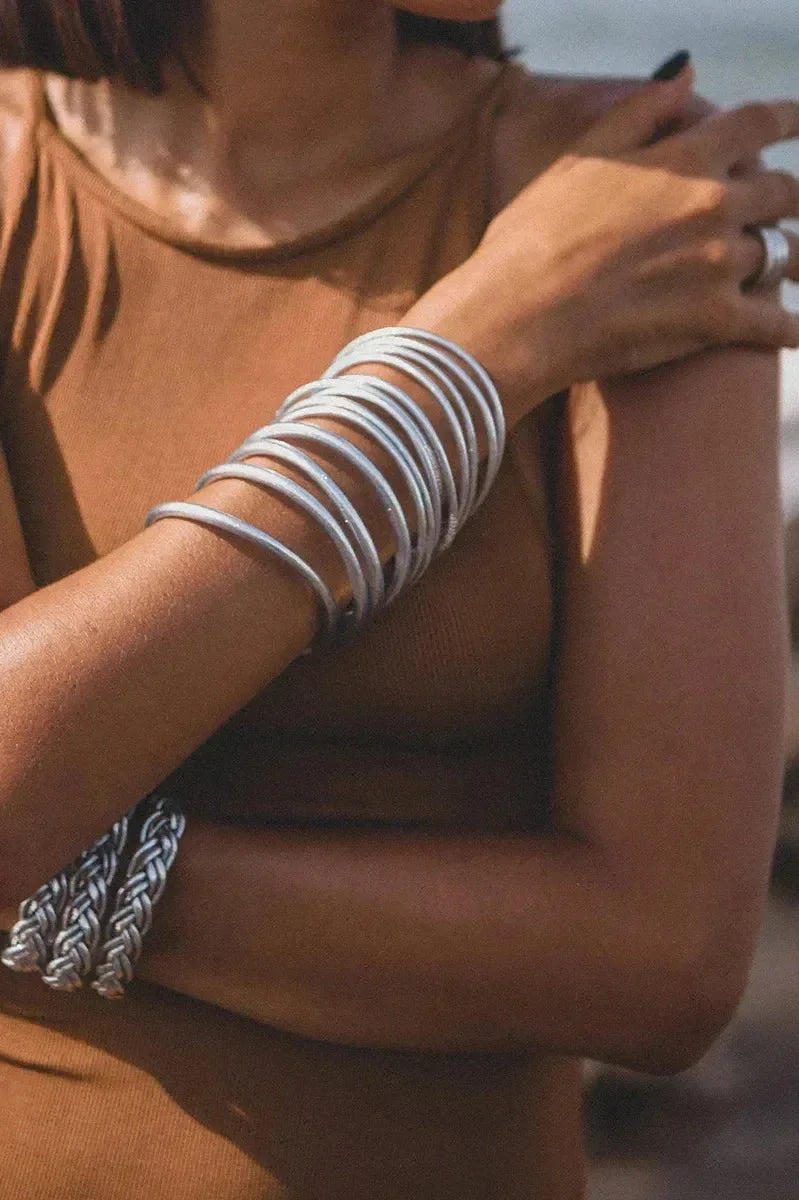 Goldene und silberne Armreifen am Handgelenk einer Person auf hellem Holzfußboden – eleganter Schmuck für Damen, modernes Armband-Design