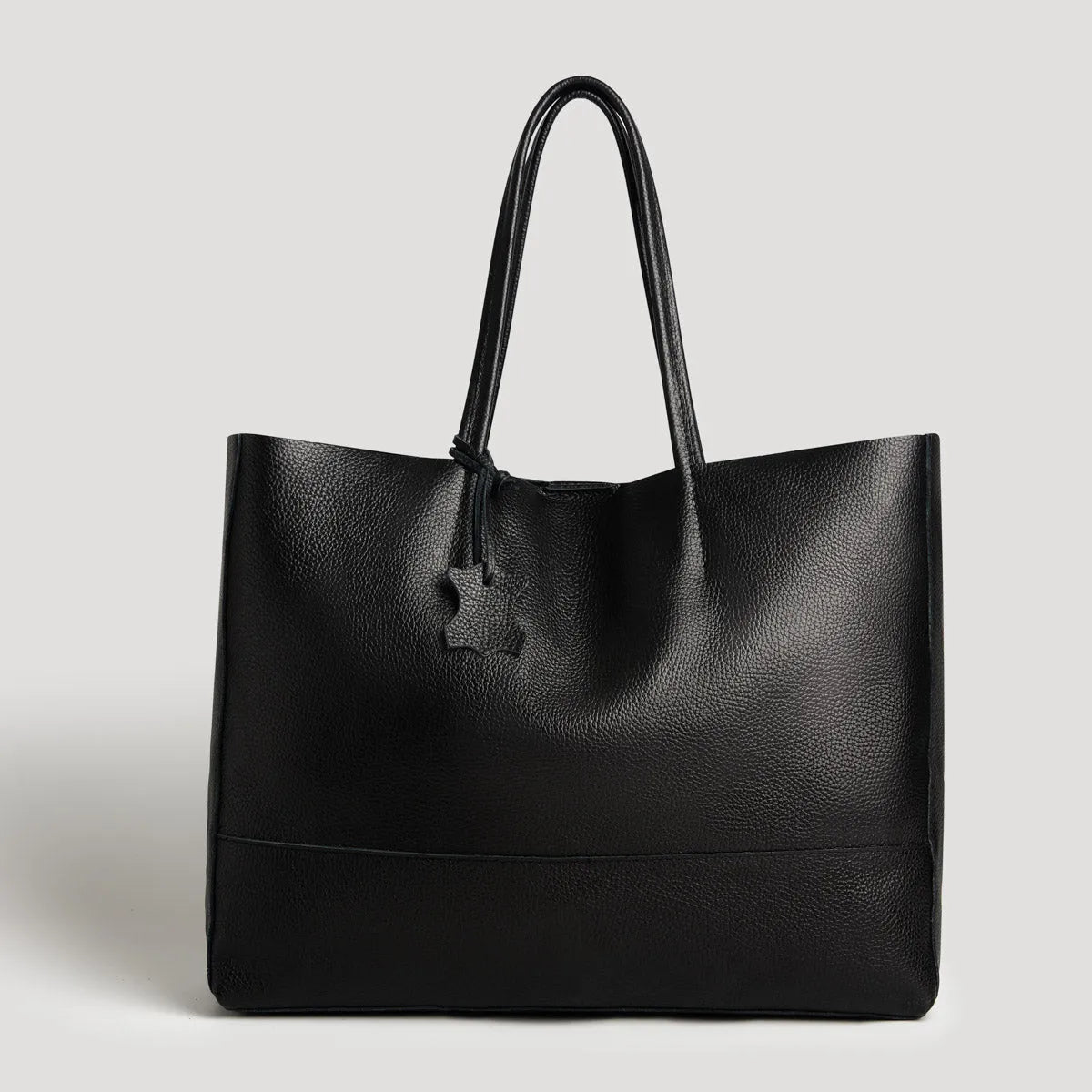 Die Umhängetasche "Susi" von flyliving aus schwarzem Leder präsentiert sich mit zwei Schulterriemen und einem Sternanhänger vor hellgrauem Hintergrund - die elegante Handtasche für Damen.