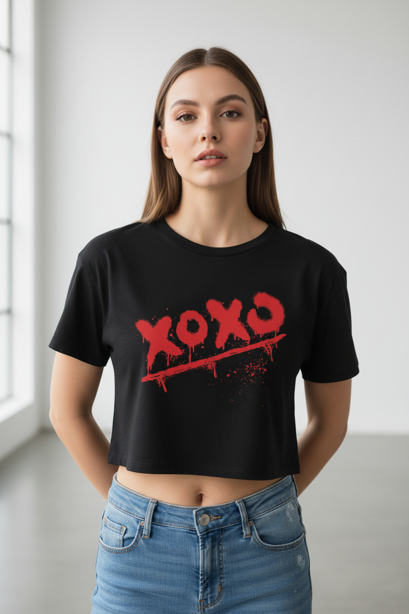 Black 100% combed cotton crop top by flyliving, featuring a red 'xoxo' spray paint graphic with drips and splatters, worn by a woman.