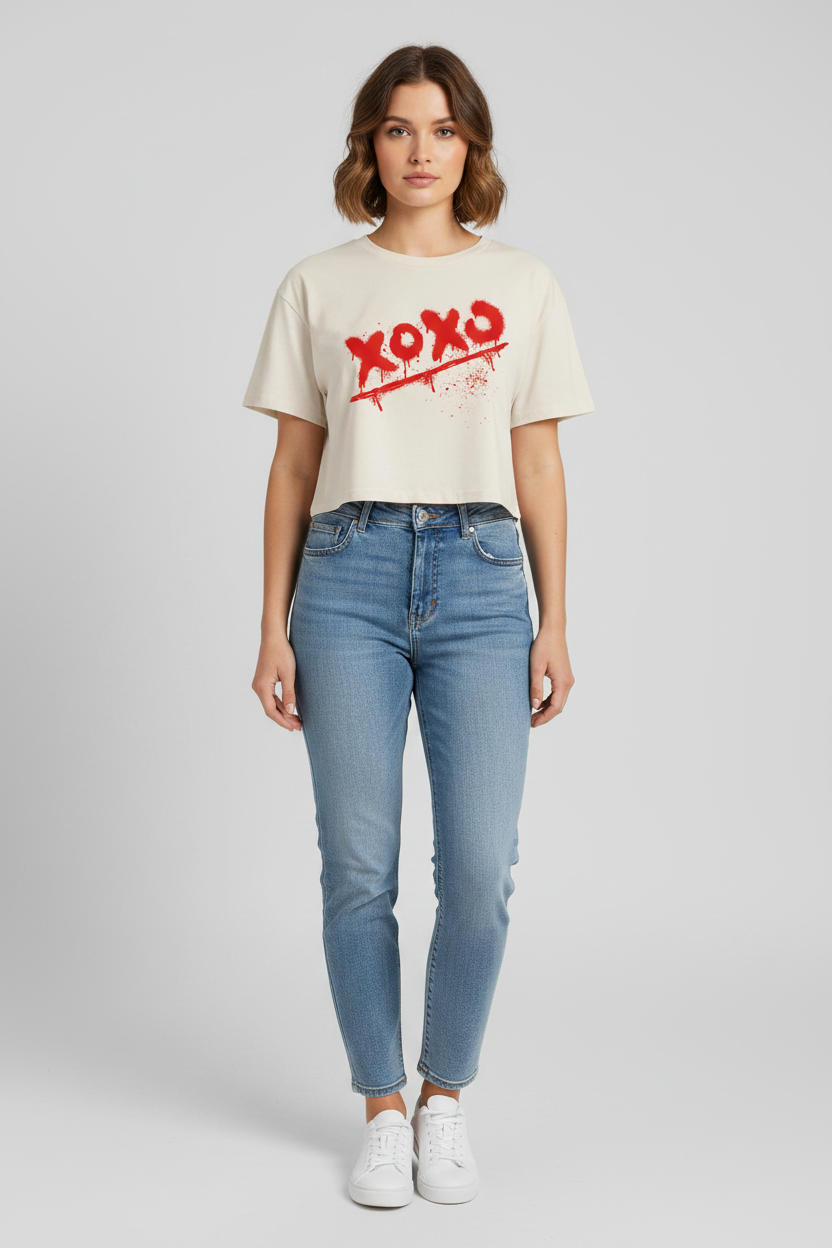 Off-white relaxed fit combed cotton crop-top by flyliving featuring a red spray-painted 'XOXO' graphic, worn with blue jeans and white sneakers.