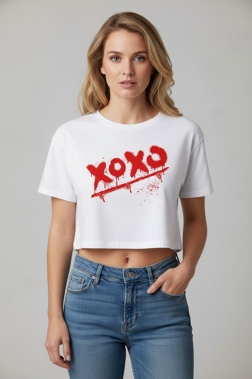 White cotton crop top by flyliving with red "xoxo" graffiti print, worn with blue jeans.