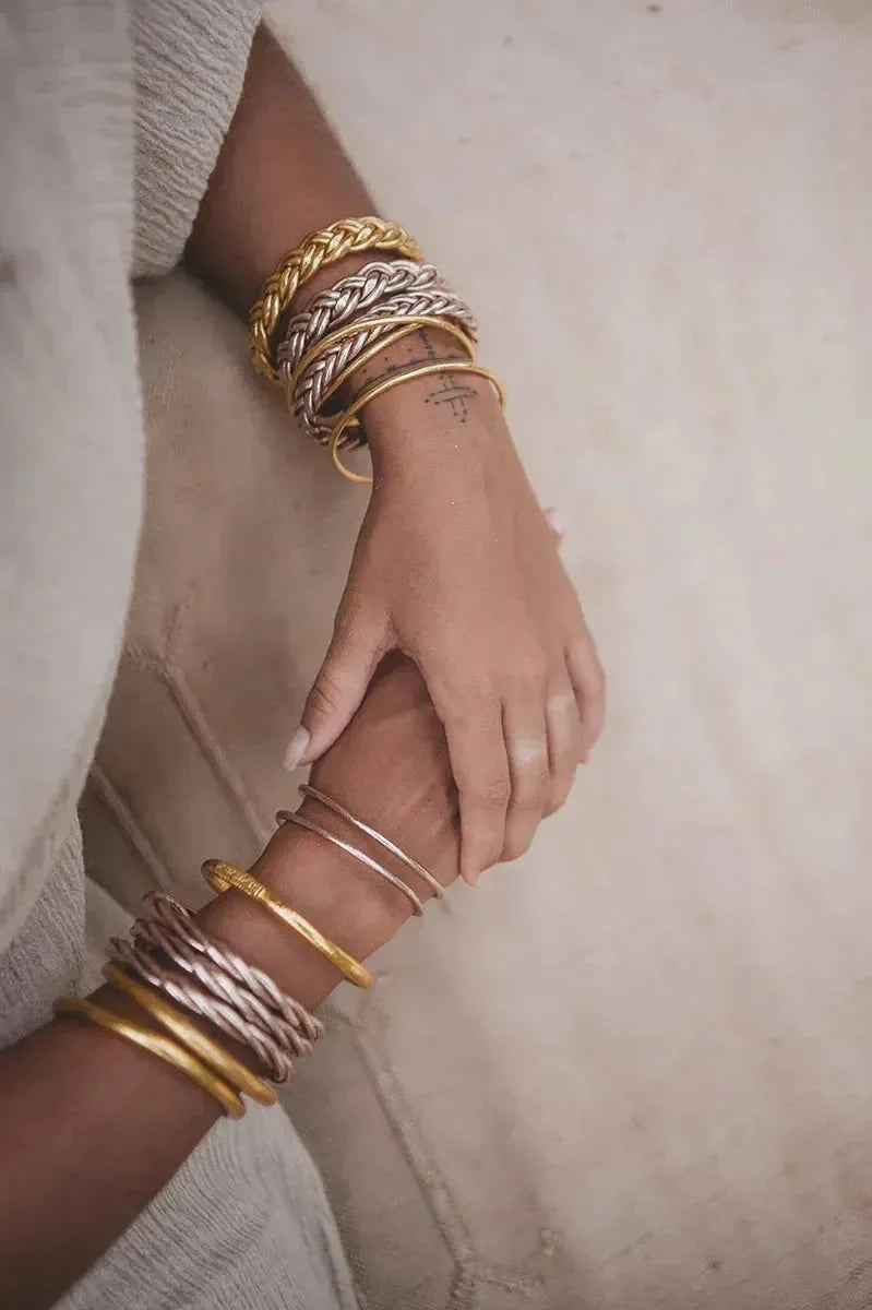 Goldene und silberne Armreifen am Handgelenk einer Person auf hellem Holzfußboden – eleganter Schmuck für Damen, modernes Armband-Design