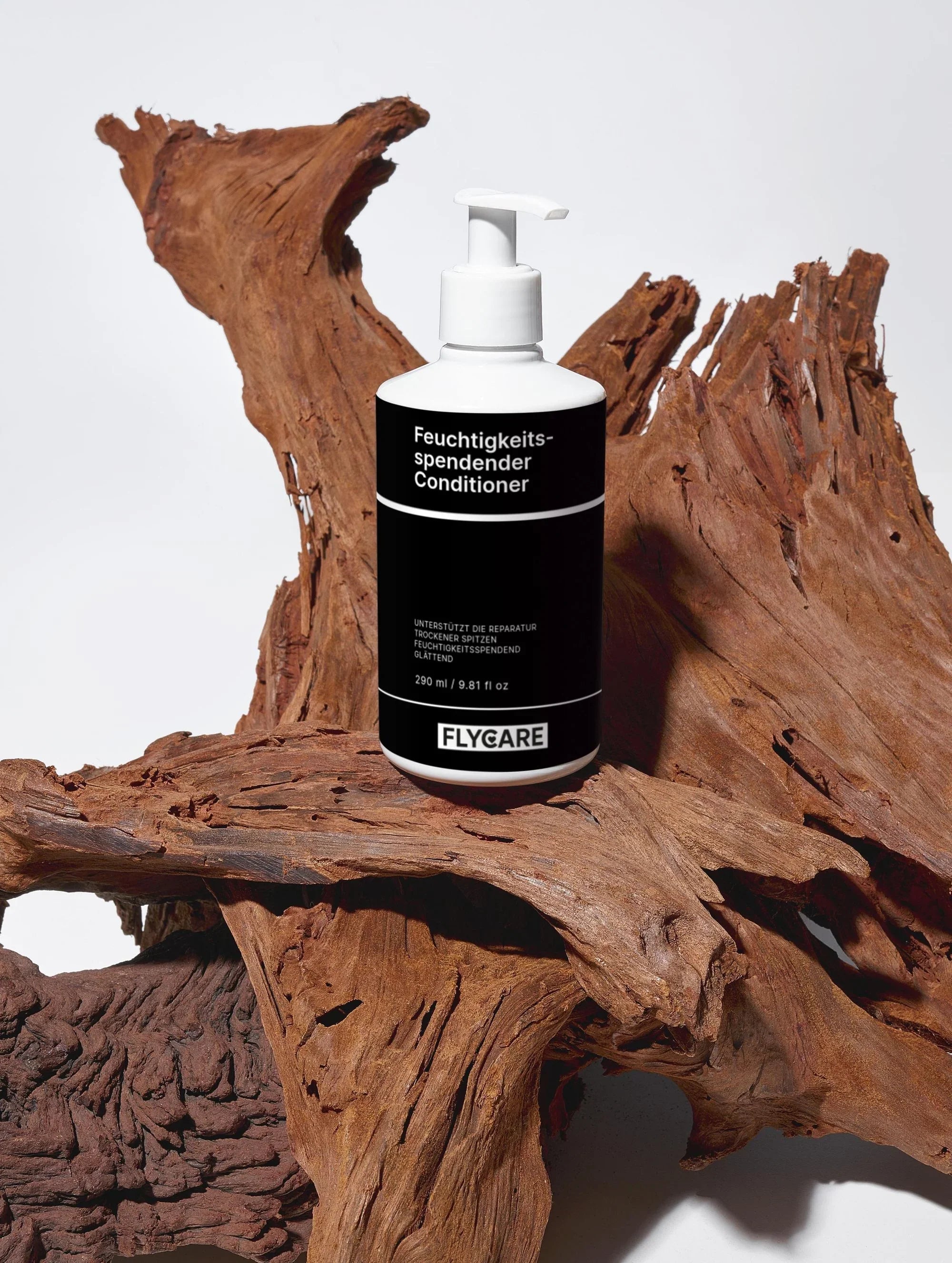 Feuchtigkeitsspendender Conditioner von FLYCARE, auf einem Stück naturbelassenem Treibholz mit rauer Textur platziert.
