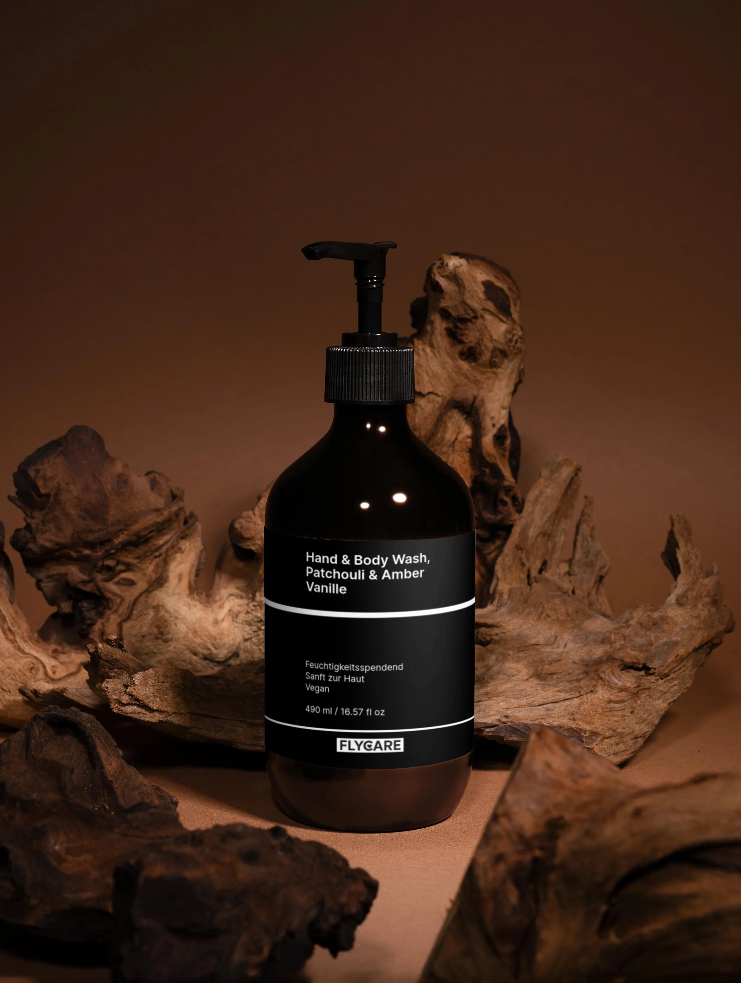 Braunes Hand- und Körperwaschgel mit Patchouli & Amber Vanille von Flycare, umgeben von dekorativem Treibholz auf braunem Hintergrund.
