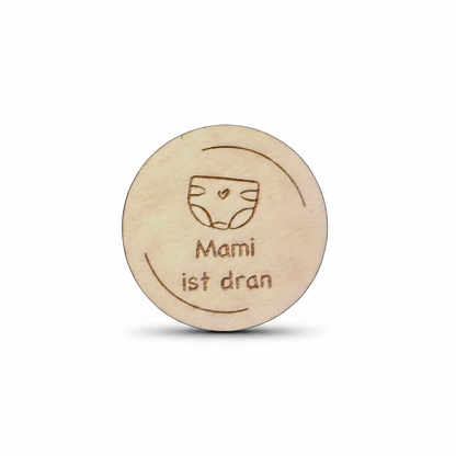 Runde holzentscheidungsmünze mit lasergraviertem windelmotiv und dem schriftzug mami ist dran für eltern