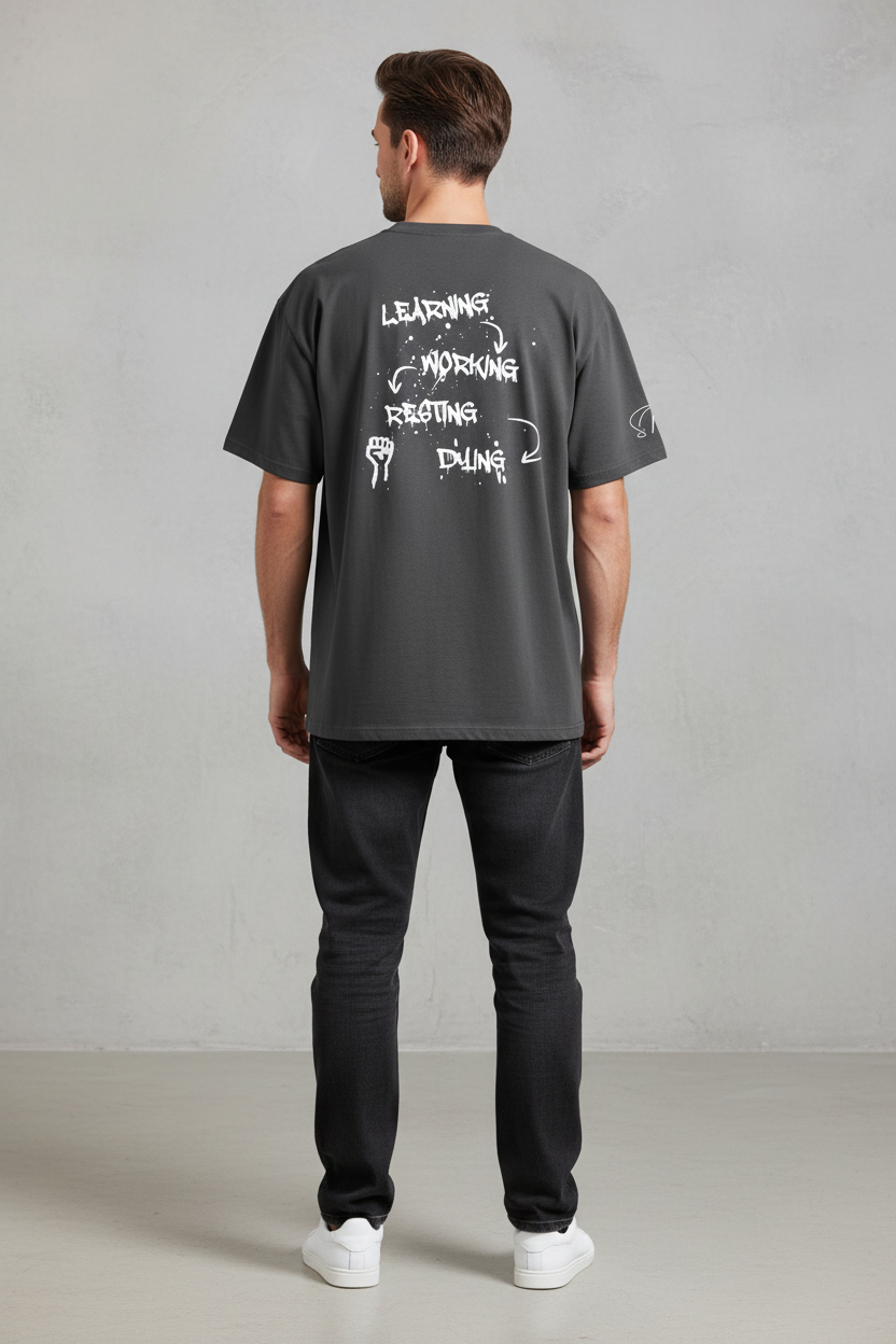 Oversized dark grey washed cotton t-shirt by flyliving, featuring a white graffiti print depicting a cycle of 'LEARNING, WORKING, RESTING, DYING' and a fist graphic on the back.