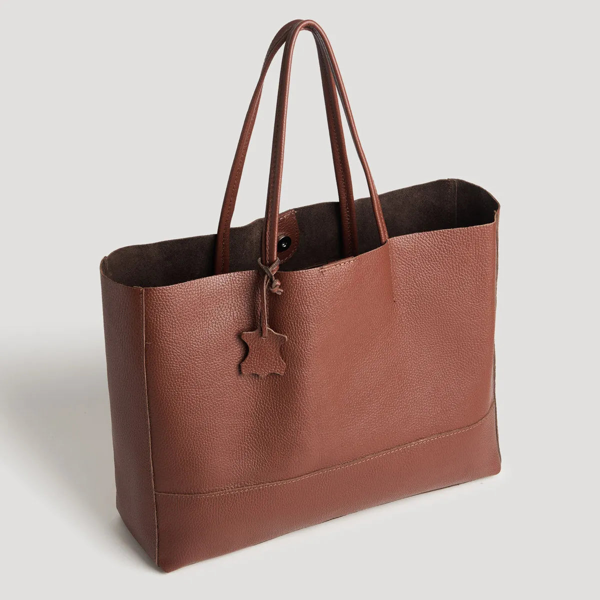 Die flyliving Umhängetasche "Susi" aus dunkelbraunem Leder mit zwei Griffen, strukturierter Oberfläche und kleinem, sternförmigem Anhänger ist ein elegantes Damen-Accessoire vor hellem Hintergrund.